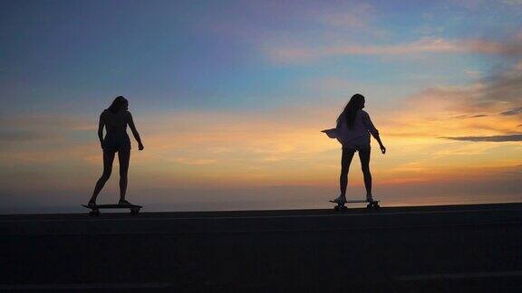 在大海和日落天空的背景下两个女孩踩着滑板的剪影