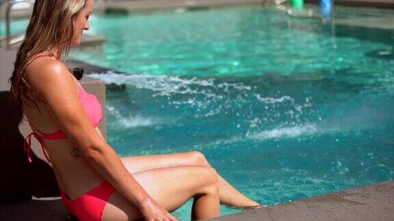 穿着比基尼的女人顽皮地踢她的脚在游泳池的水