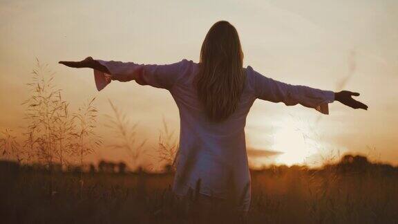 日落时分一名身穿白衬衫的年轻女子在田野中央举起双臂