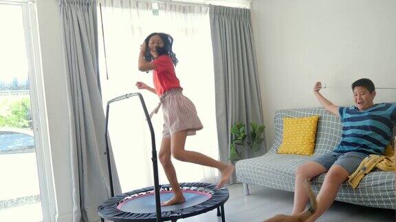 快乐的亚洲女孩在家里的迷你蹦床上跳她的弟弟在窗户附近和狗玩生活理念
