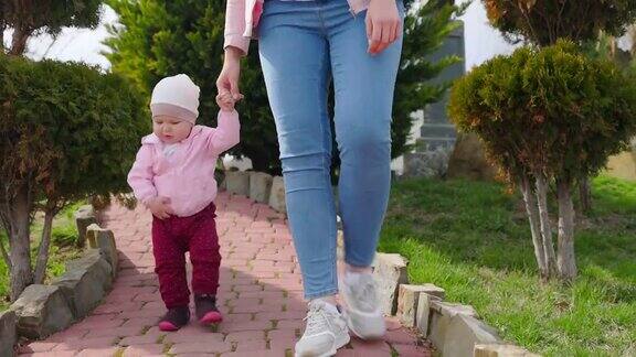 第一个步骤婴儿学着和妈妈手拉手走路从较低的角度看孩子的特写