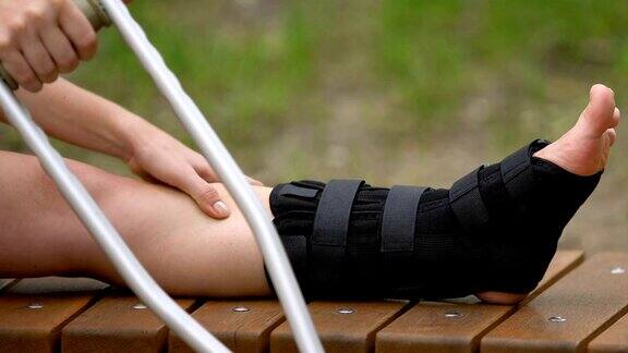 女性患者在户外用拐杖按摩疼痛的腿
