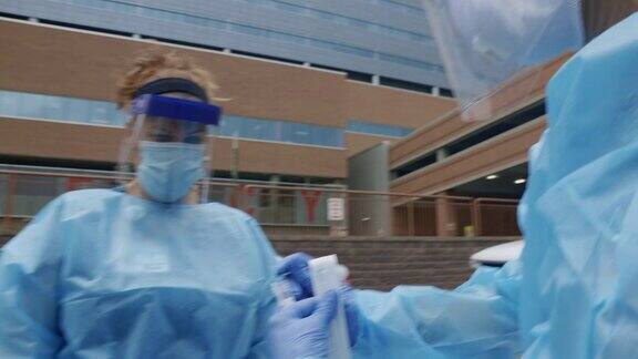 在诊所医院外的COVID-19检测线上一名身穿长袍、戴着外科口罩、手套和面罩的女护士将用过的棉签放入另一名护士手持的无菌试管中