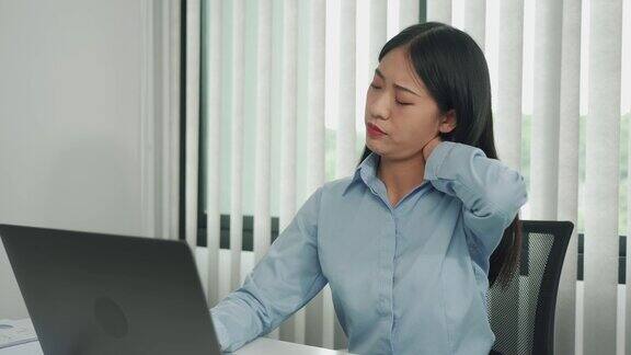 一位年轻的亚洲女性正坐在公司的办公室里脖子很疼