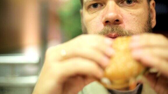 一名蓄着胡须的白人男子晚上坐在一家夏日咖啡馆的桌边吃着汉堡包关闭了