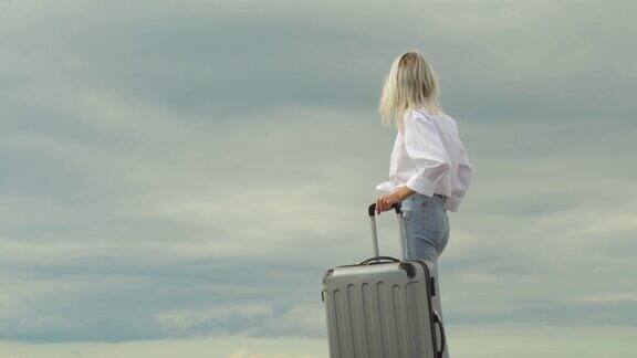 一个美丽的女人拿着一个手提箱在大海的背景下