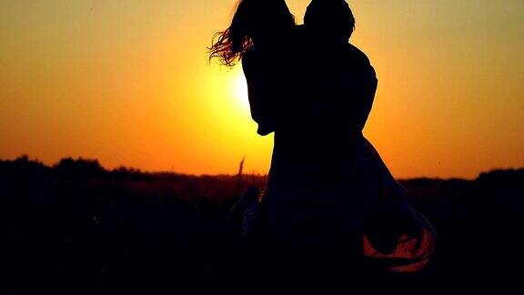 一对夫妇的剪影拥抱在幸福旋转的场地在日落