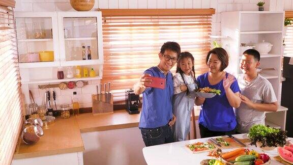 幸福的亚洲家庭准备烹饪健康的食物和自拍与智能手机在厨房家庭放松和花时间在一起在家里