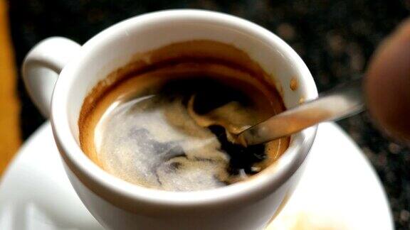 用金属茶匙混合黑热的特浓咖啡和蓬松的泡沫