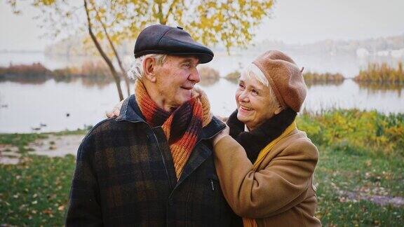 一对退休的夫妇祖父母在河边的城市公园里聊着笑着相爱地看着对方