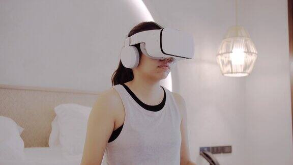 亚洲女性在家里的卧室里使用VR眼镜锻炼身体