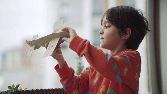 男孩在家阳台上玩纸飞机纸飞机儿童驾驶手工飞机一个学生做了一个纸飞机并玩它