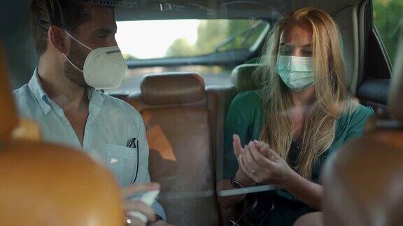 一名男子和一名女子戴着防护口罩坐在出租车后座用杀菌剂消毒双手
