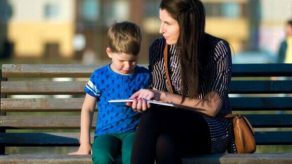 年轻的母亲和儿子坐在公园的长椅上看书