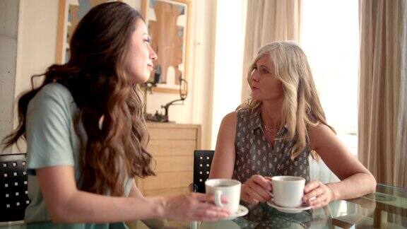 母亲和成年的女儿在家里一边喝咖啡一边聊天
