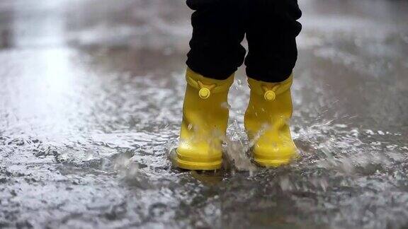 穿着黄色橡胶靴子的孩子的腿在水坑里跳