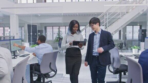 两位年轻的男性和女性专家拿着平板电脑走进办公室无视同事只顾讨论工作现代开放式办公室中积极的多样化业务经理