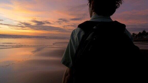 夕阳西下一名男子背着双肩包沿着海滩漫步