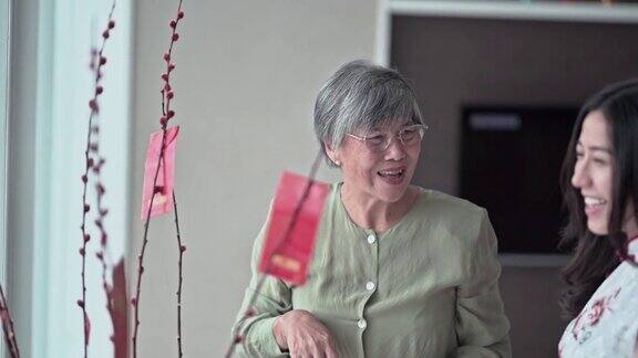 中国新年老奶奶和她的女儿装饰房子客厅用柳树和红包装饰准备家庭团聚