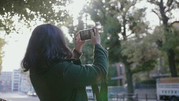 一名女性在秋天用智能手机拍照