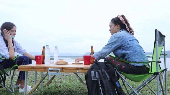 两个亚洲女人在湖边露营的时候一起喝着啤酒