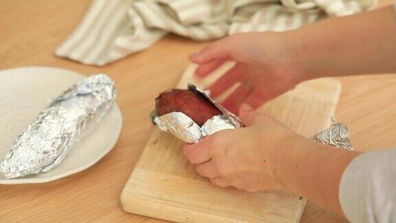 一名妇女打开用锡箔纸做成的烤红薯桔子库马拉红薯