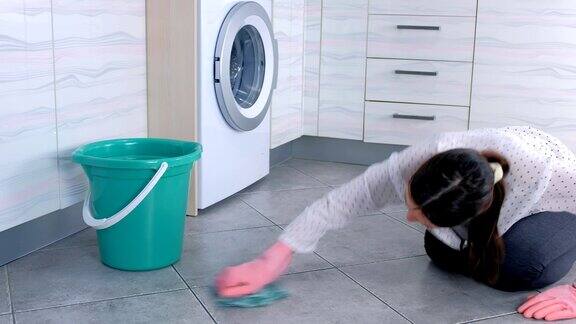 穿着粉红色橡胶手套的疲惫的女人用一块布擦洗厨房地板上的污渍