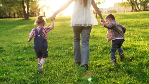 日落时分母亲和孩子们手牵着手一起在草地上奔跑