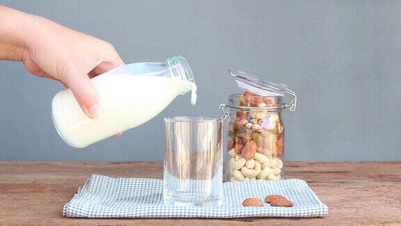 女人把牛奶倒进一只玻璃杯和一瓶干果木桌上放着各种坚果