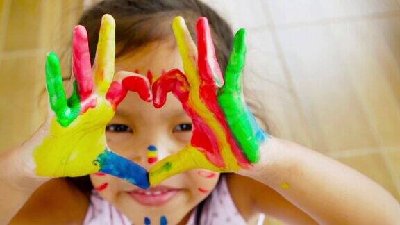 特写的亚洲女孩做一个心形手势与彩色绘画她的手慢动作拍摄100帧秒