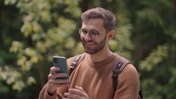 一个男人走在树林里用手机写了一条信息一名背包旅行者在徒步旅行时用手机打印了一条信息