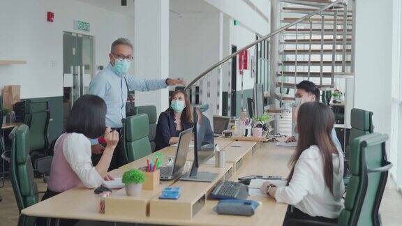 工作中的亚洲华人高级同事戴着口罩回到办公室早上在办公室互相问候