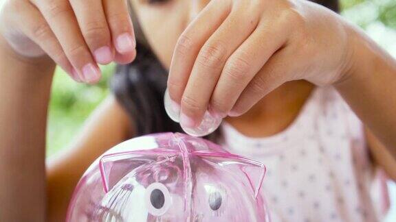 亚洲小女孩把硬币放进小猪储蓄罐