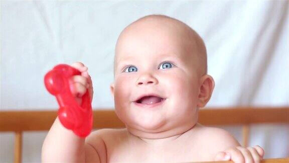 宝宝微笑着看着镜头站在床上拿着玩具