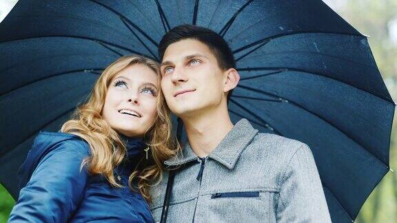 一对年轻夫妇站在一把伞下:在下雨