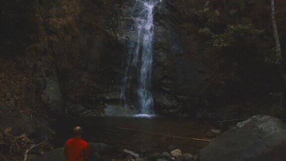 航拍男子坐在隐藏在森林里的美丽瀑布前
