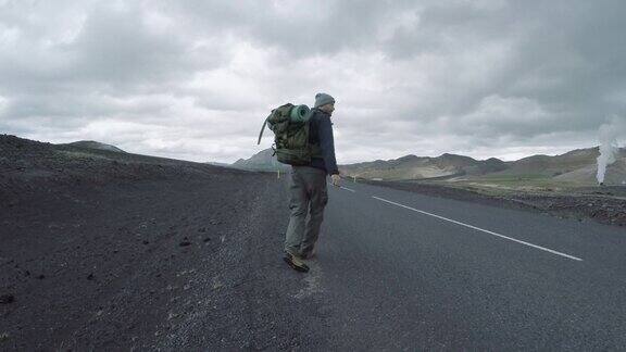 背包游客沿着冰岛荒凉的公路搭便车