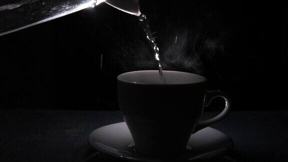 水从茶壶倒进杯子蒸汽滴在黑色背景上剪影杯子里放一杯热饮