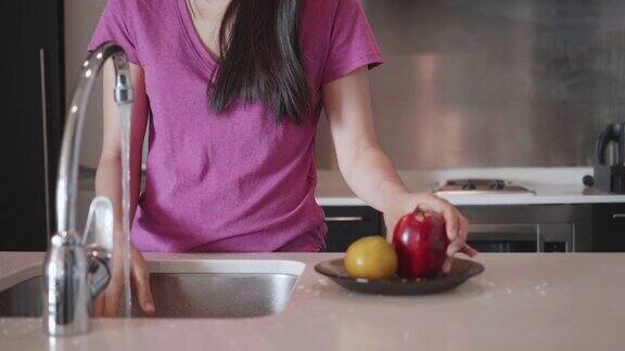 年轻女子在家里的厨房水槽里洗盘子和水果