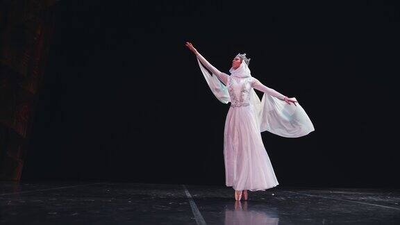 一位优雅、勤奋的芭蕾舞演员在黑色背景上表演美丽的芭蕾元素风吹着她美丽的白色套装缓慢的运动