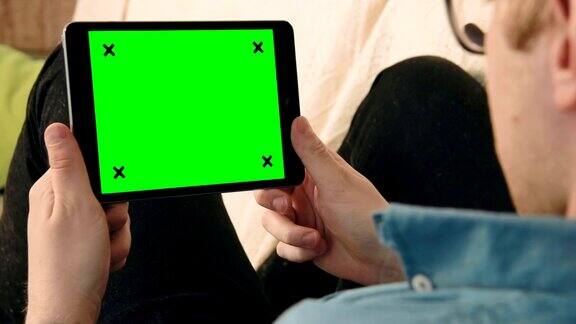 年轻人躺在沙发上看绿色屏幕的数字平板电脑