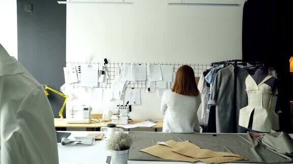 年轻设计师背对着镜头看着挂在墙上的画女士正在考虑新的服装收藏