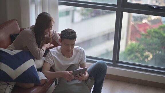 一对亚洲中国年轻夫妇周末一起在客厅看数字平板电脑