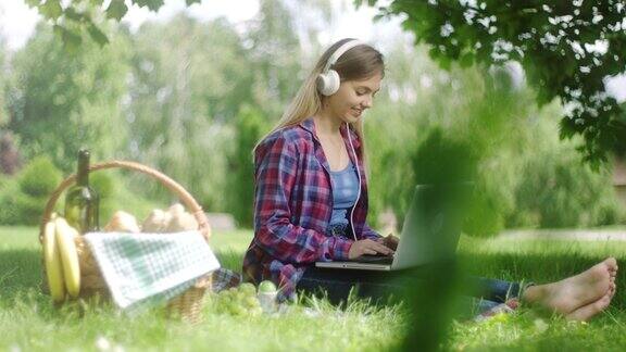 一个女人在野外用笔记本电脑和耳机野餐