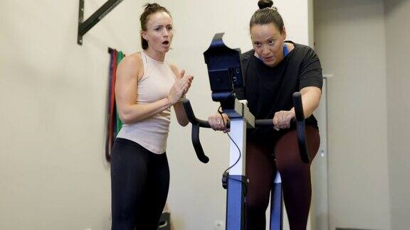 中年妇女做有氧运动在健身房自行车健身教练