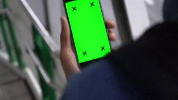 一名男子走下楼梯使用绿色屏幕的手机