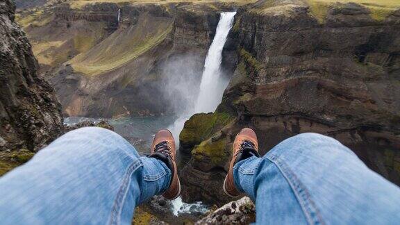 一个人坐在悬崖上看着峡谷里的瀑布