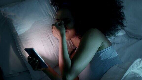 年轻黑人女性在床上用智能手机发短信