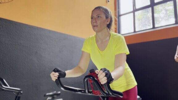 美丽的女人在健身房的动感单车课上流汗