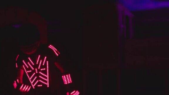 在黑暗的室内或俱乐部里穿着发光服装的人在五颜六色的led灯下跳舞和移动穿着身上有霓虹灯的衣服跳舞的舞者由ARRIALEXA电影摄像机拍摄